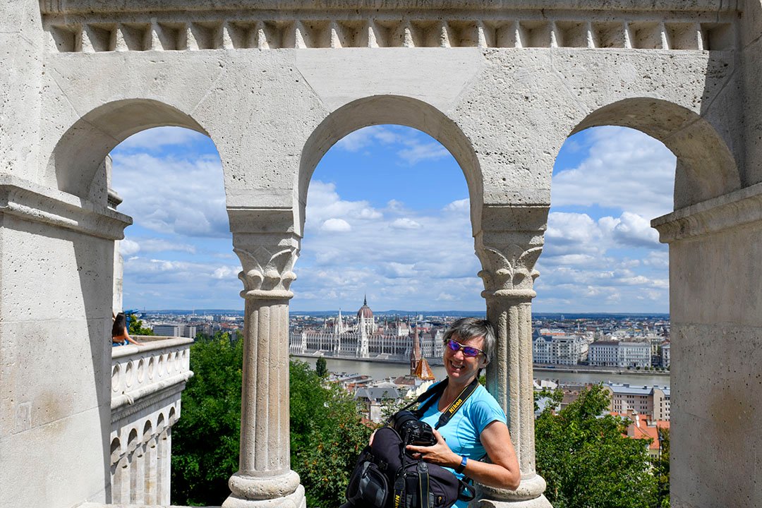 Photographer leaning  against the arches of Fisherman's Bastion with Budapest Parliament in the Background