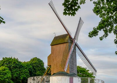 Historic Windmill on top of hill with green grass and a path located in Bruges Belgium